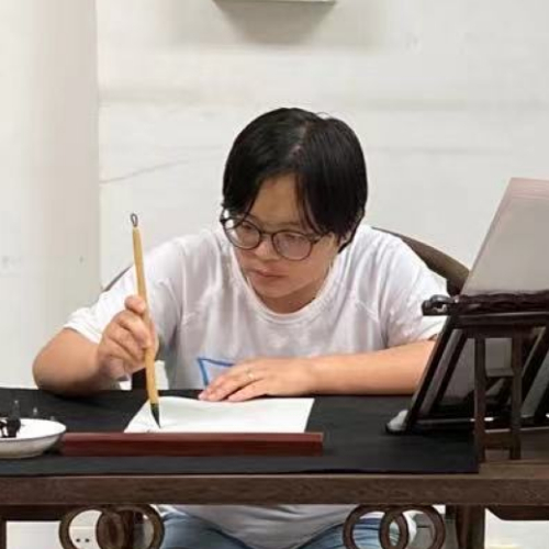 Li Zhang Asian person with glasses holds a calligraphy pen