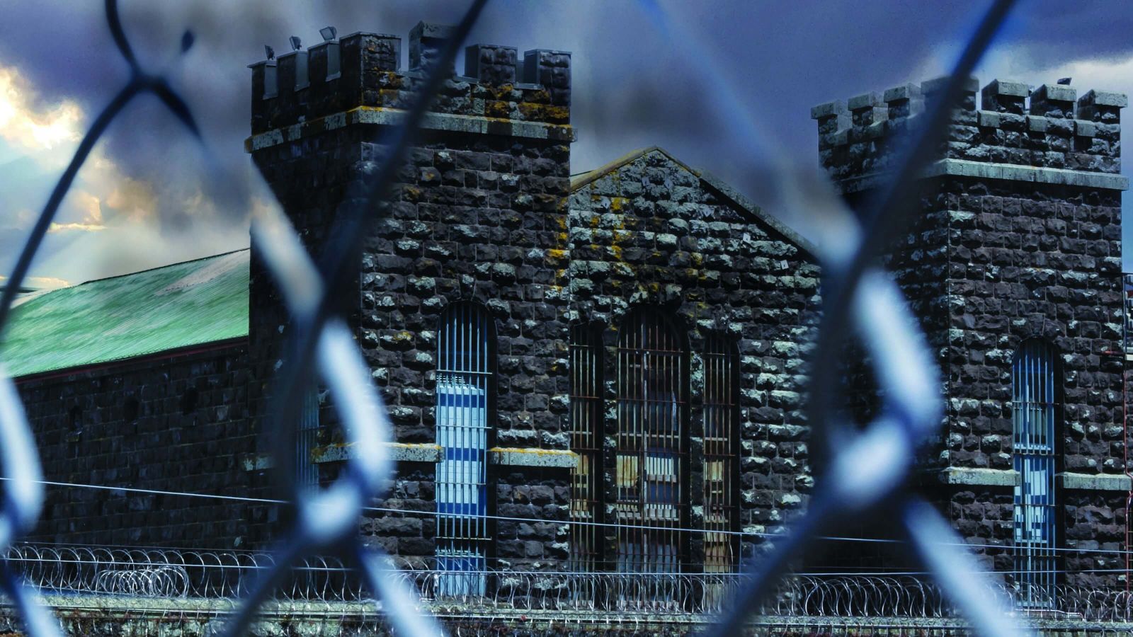 Looking through a fence at the front of a dark and grey prison building