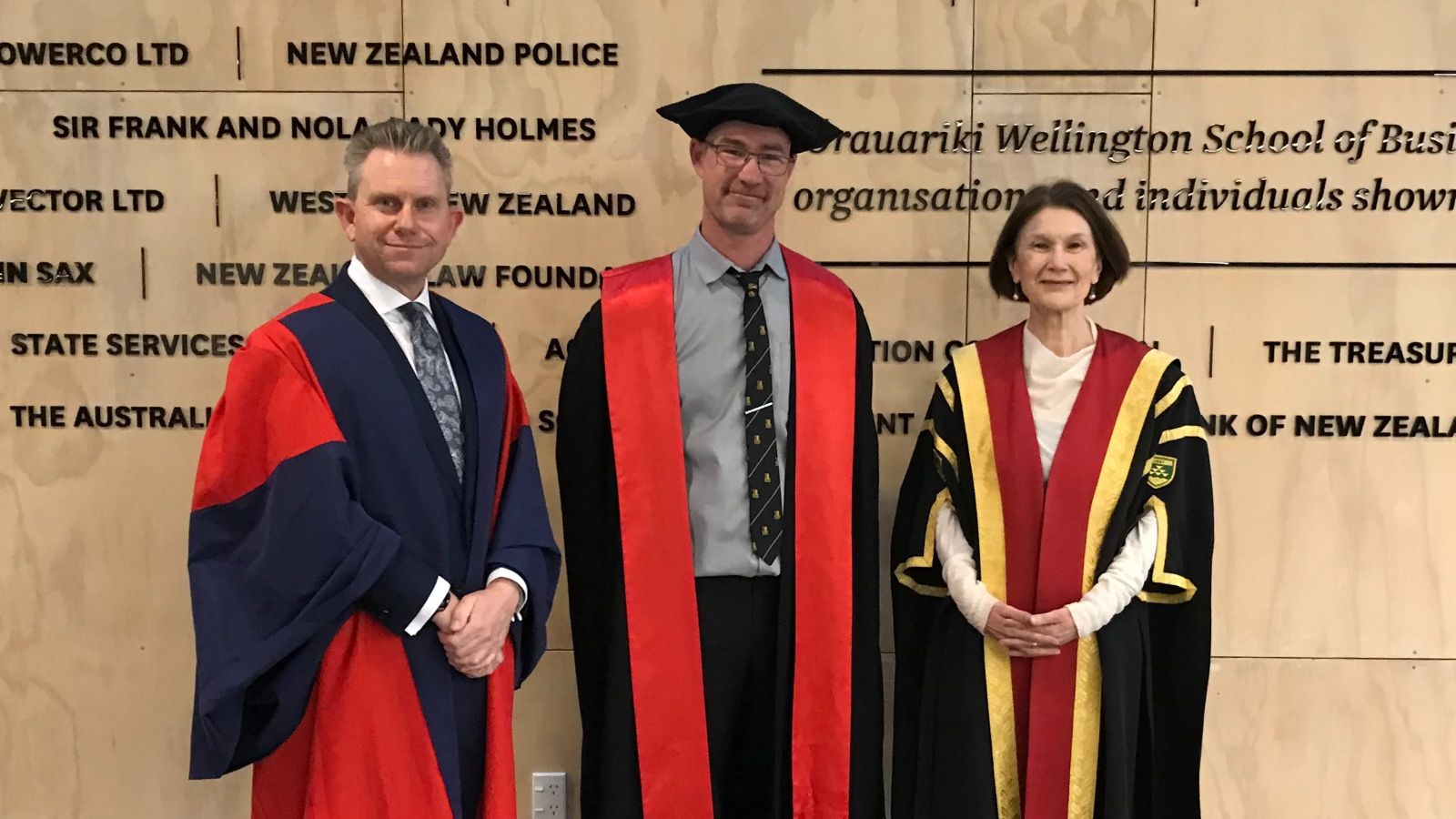 Three academics wearing robes in front of a wall showing sponsors of the Business School, from left to right Mark Hickford, John Randal, and Jennifer Windsor