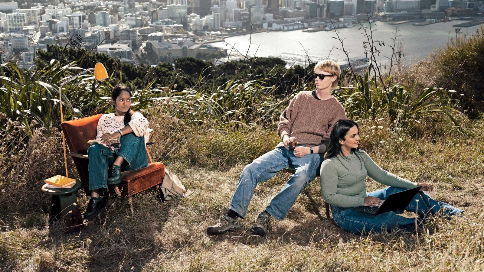 three students hanging out on chairs at the top of a hill that looks out to the city and harbour 