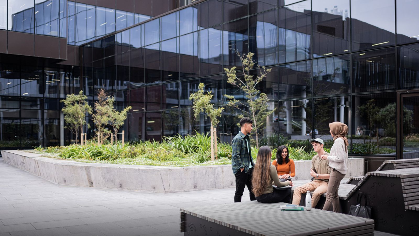 5 students gathered outside a campus building with trees in the background