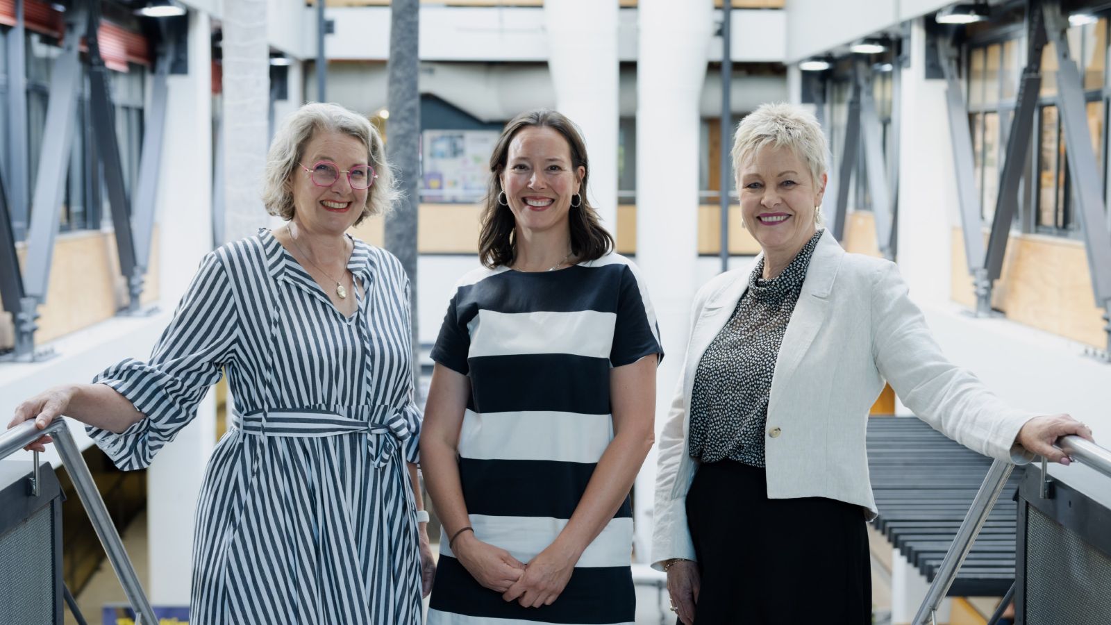 Professor Robyn Phipps, Professor Pamela Bell, and Professor Robyn Longhurst standing in front of the stairs at Te Aro campus, smiling at the camera.
