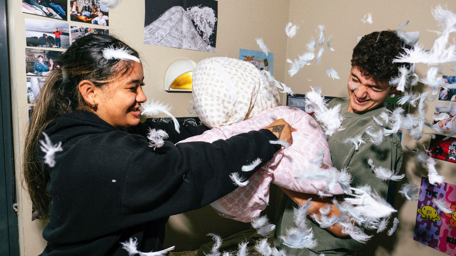 Two students in a halls of residence room having a pillow fight with feathers flying around them