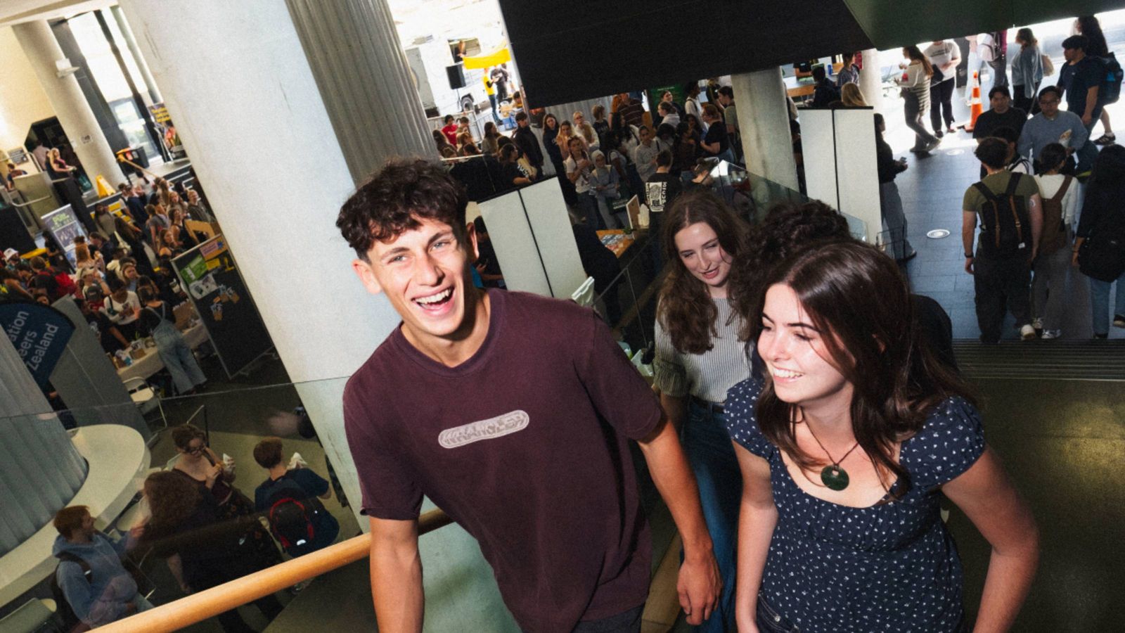 Students moving through a busy Kelburn campus during Orientation Week, with information stalls and crowds in the background