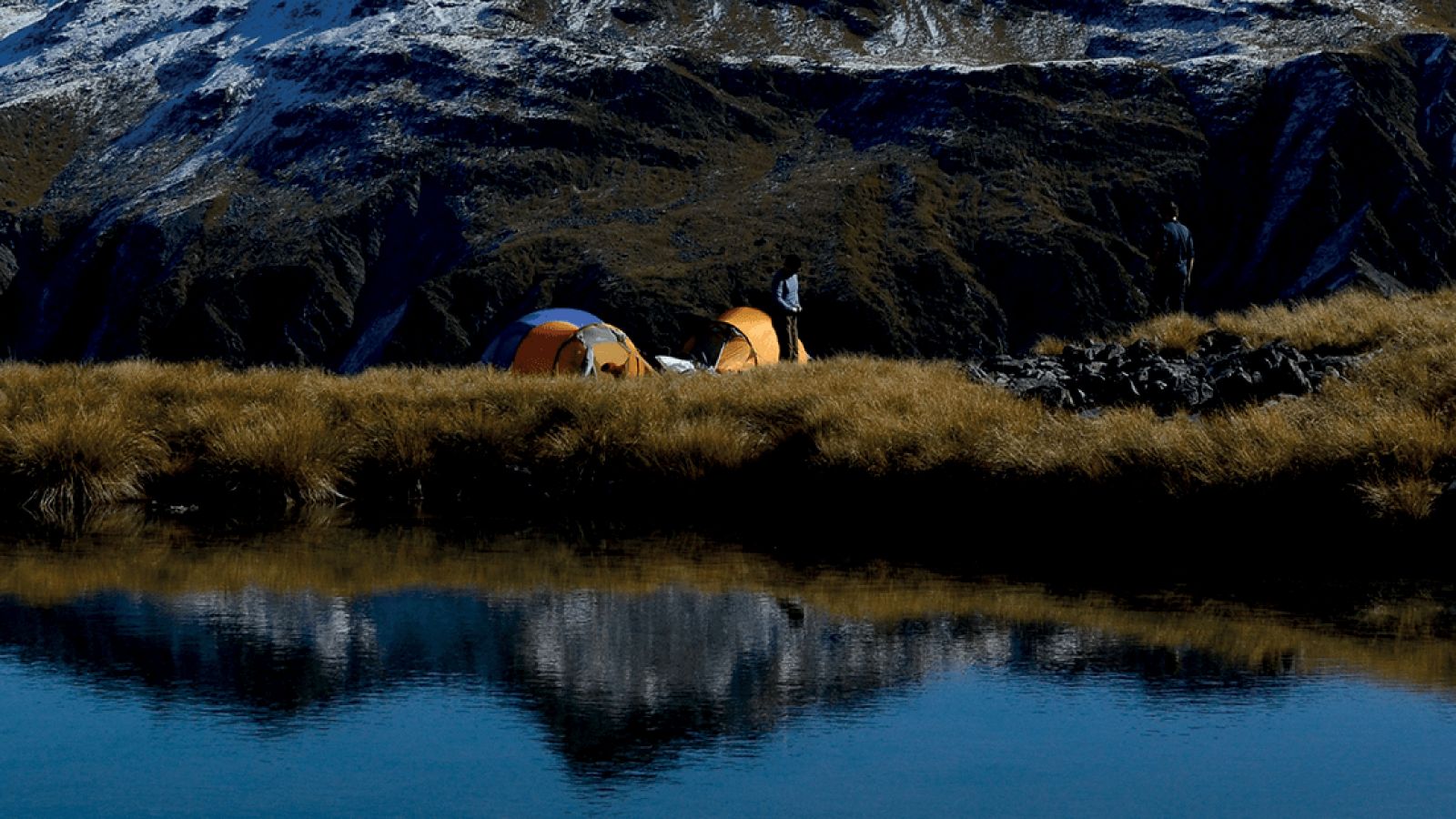 An image of two yellow tents setup by water with mountains in the background.