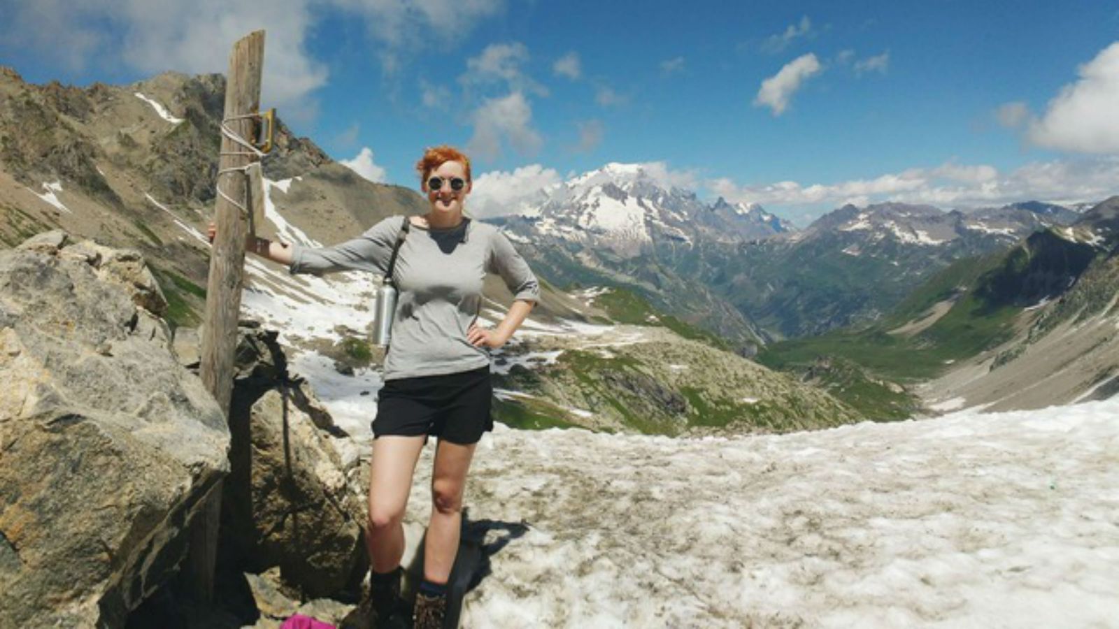 PhD candidate, Florence Isaacs stands next to a wooden box in the French Alps, with mountain scenery behind her.