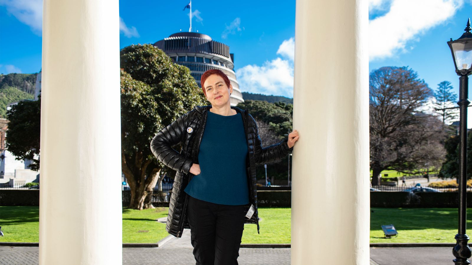 Two white shafts from columns of the Old Government Buildings frame New Zealand Parliament from the foreground, and between them rests Professor Claudia Geiringer.