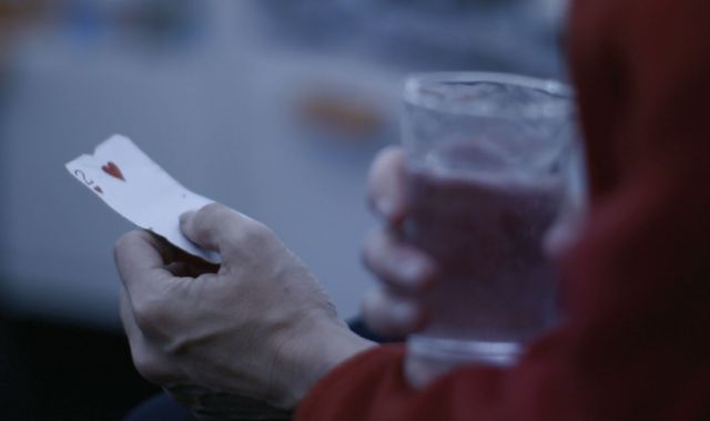 A still from the short film 'Night Shift' – a hand holds a card that shows the 2 of hearts and the other hand holds a cup of cola.
