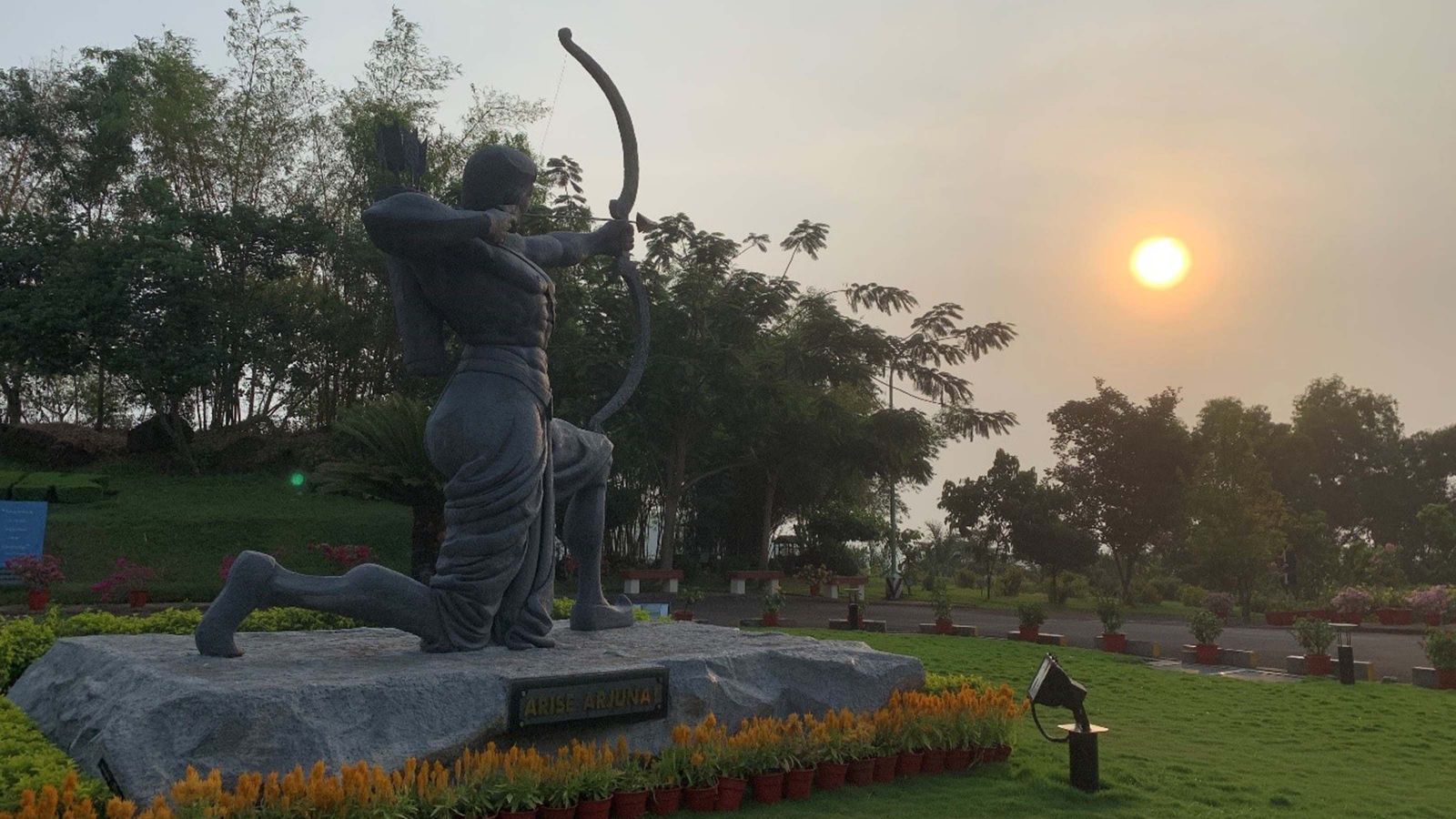 A statue of a man with a bow and arrow as the sun sets