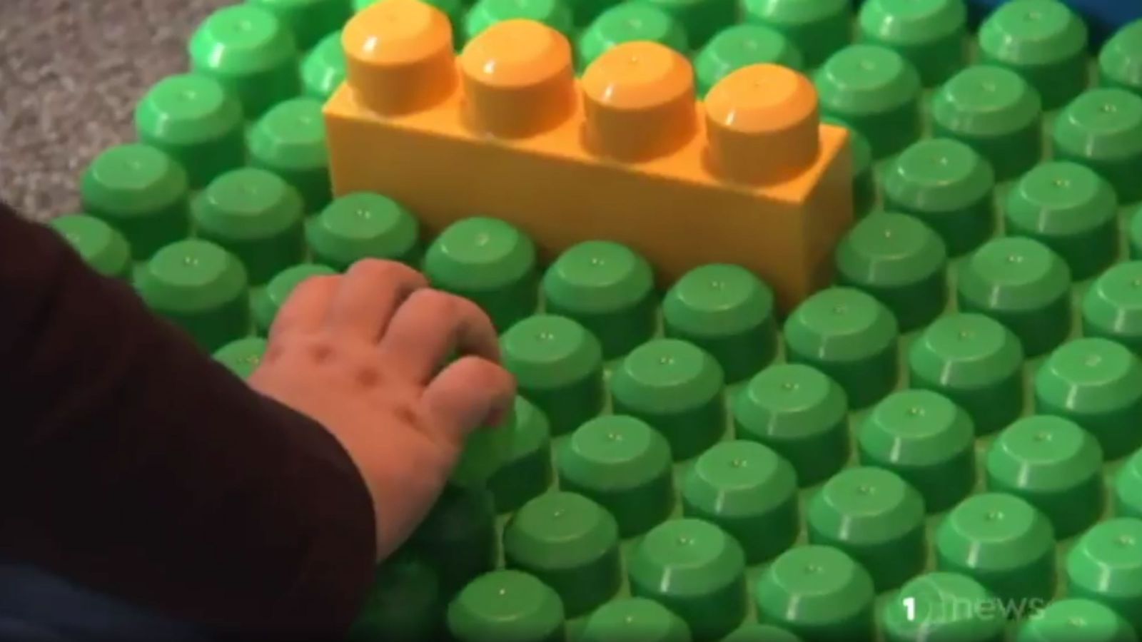 A child’s hand by a large yellow block secured on a large green block surface.