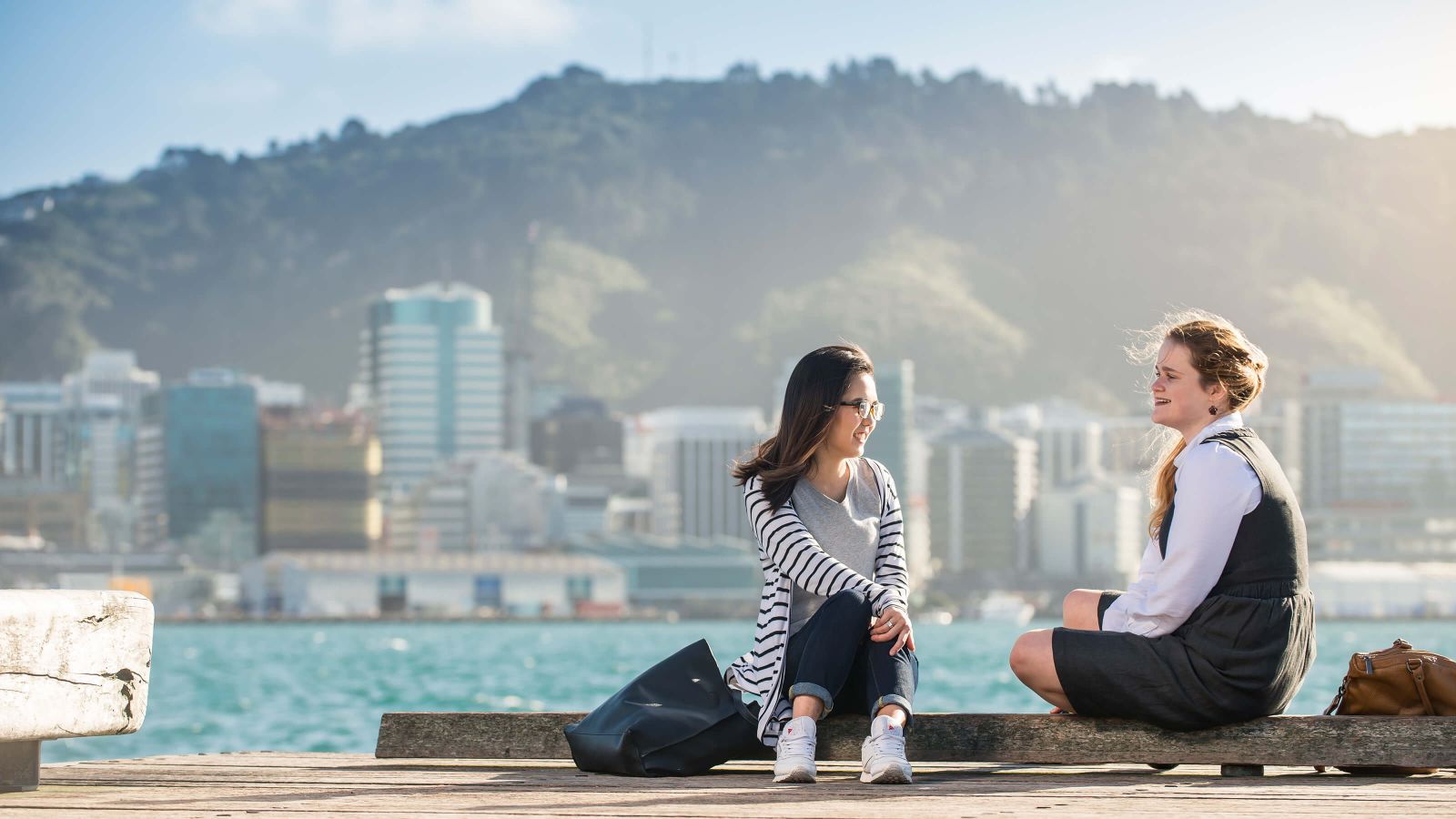 Two students by the Wellington waterfront with tall buildings of the central business district in the background.