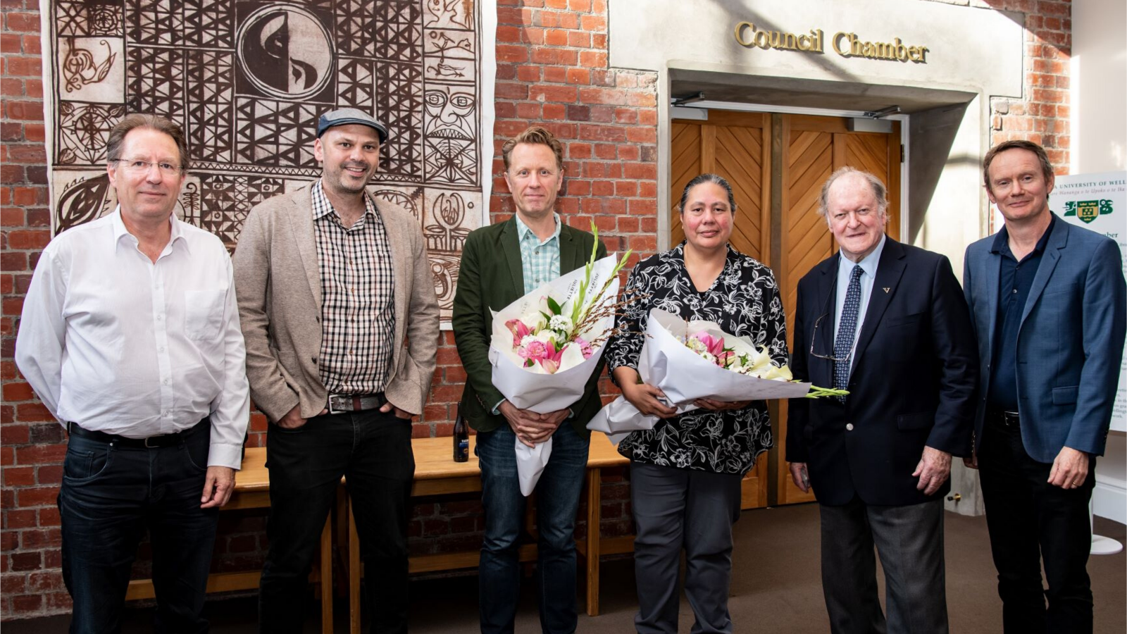 six people in front of the council chamber celebrating prizes, two with flower bouquets