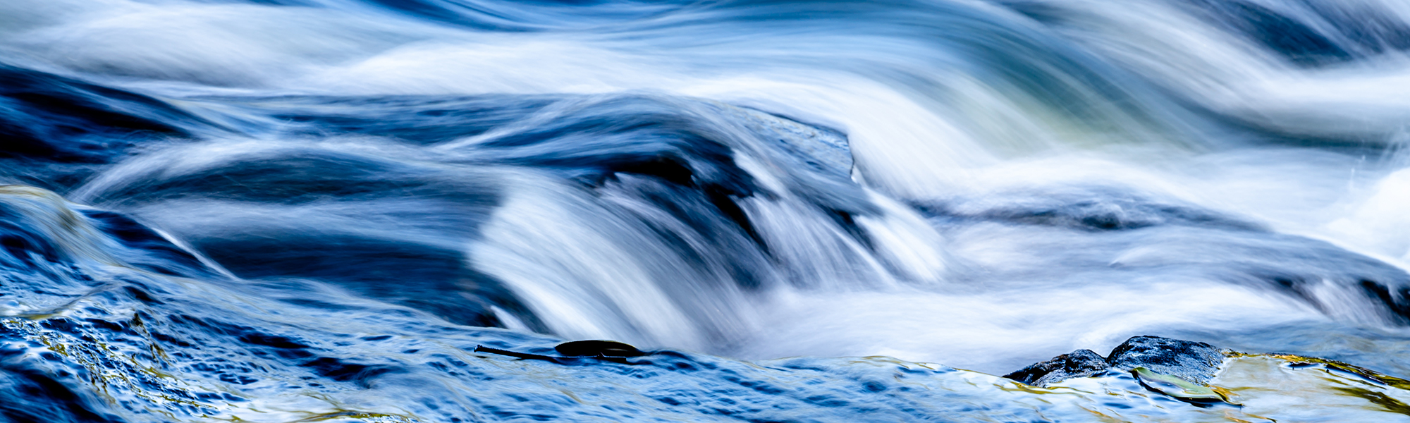 Clear blue water flows over rocks in a long-exposure photograph of a New Zealand river.