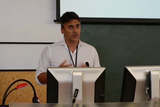 A professional man gives a presentation at the front of a lecture hall.
