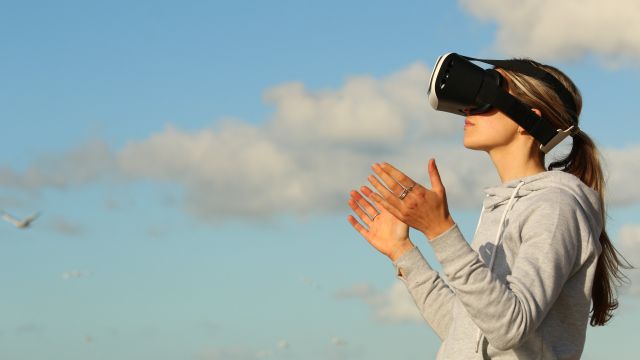 Woman wearing VR headset in front of sky with clouds