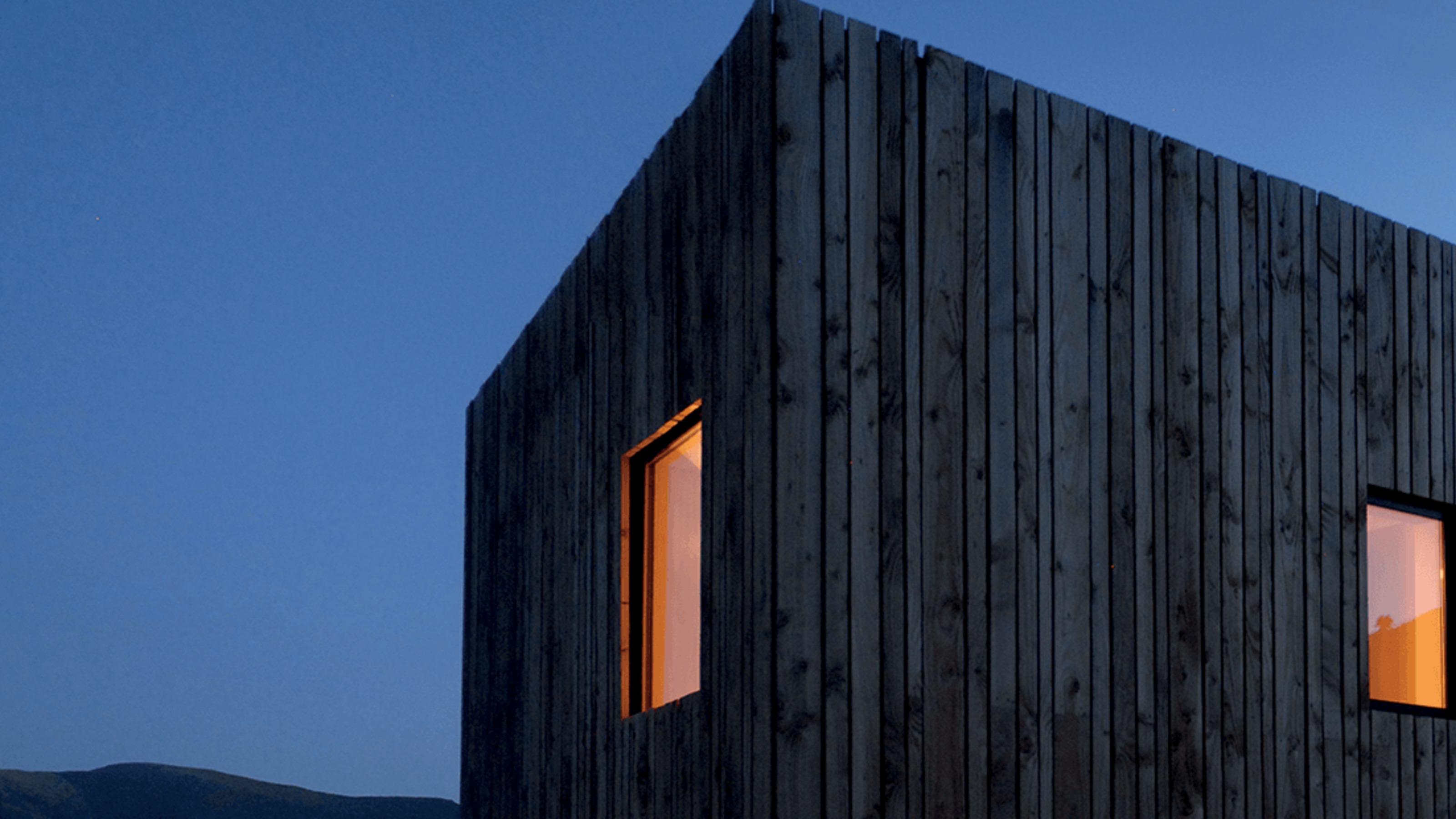 Early evening shot of dark, square modern house lit from inside