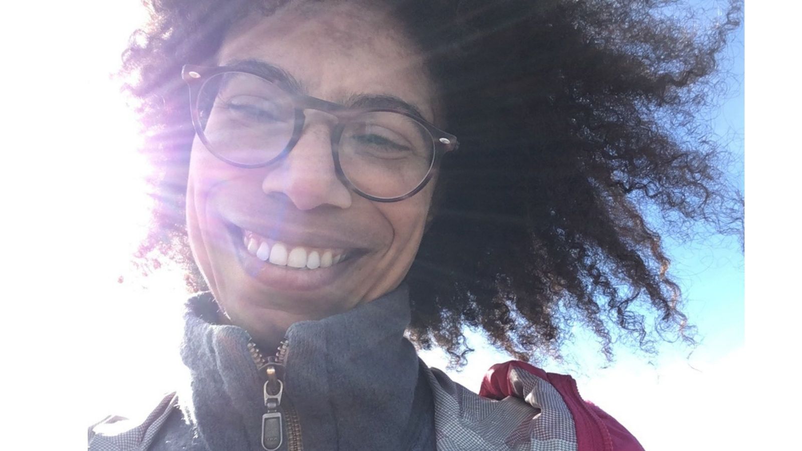 girl with curly dark hair flying smiling into camera with sun in background