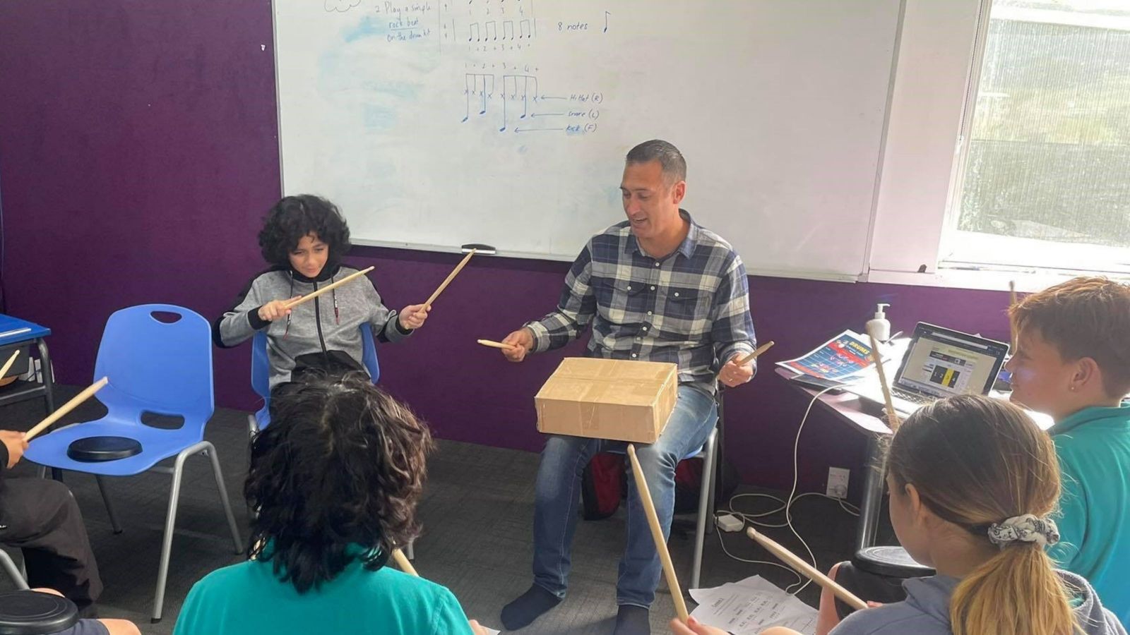 jon pirini teaching drumming man drumming on a box, kids around him also drumming on boxes