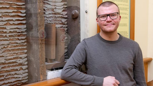 Griffin is standing in front of a display wall showing the inside of a wall.