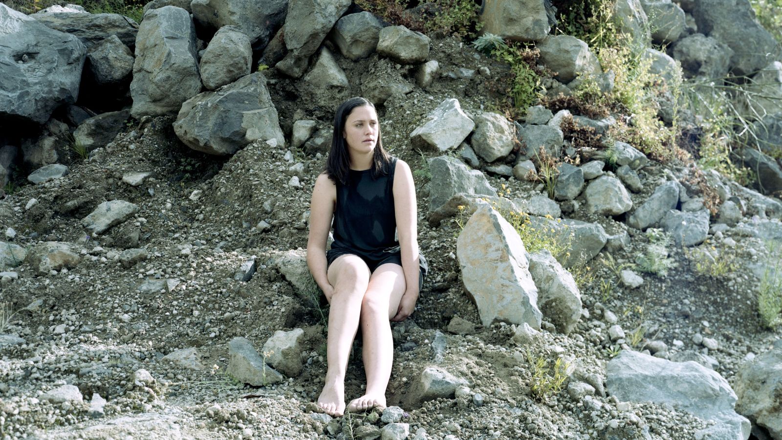 A woman sits on a rocky shore