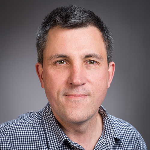 A portrait photograph of a man with short dark hair and a plaid shirt.