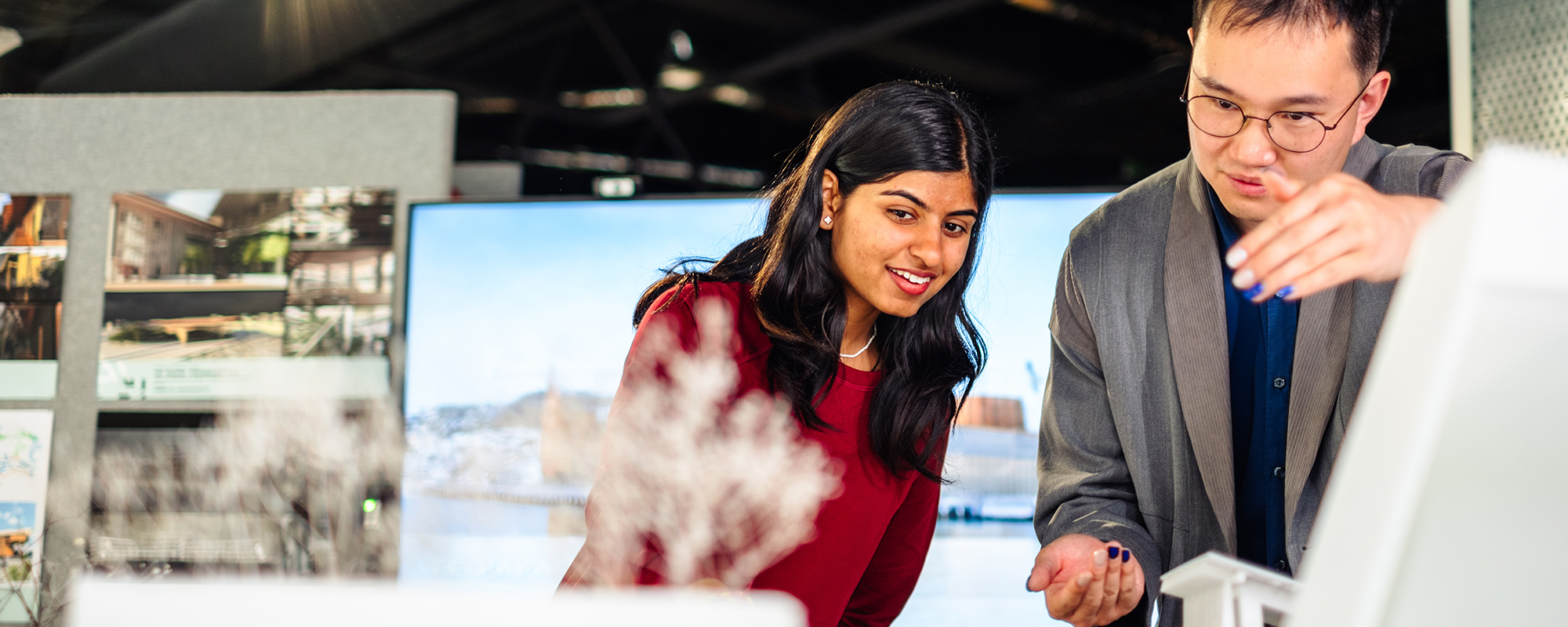 Two students surrounded by displays of other students' work, in the main atrium of the Architecture and Design school, as part of the End-of-Year Exhibition.