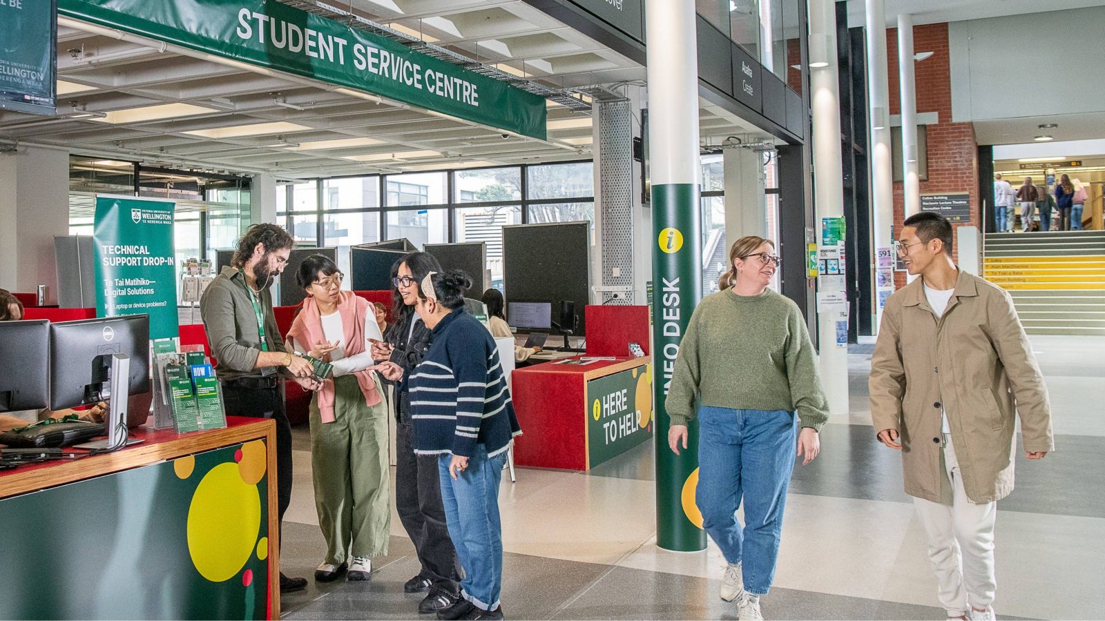 Staff and students gathering and chatting around the Info Desk 