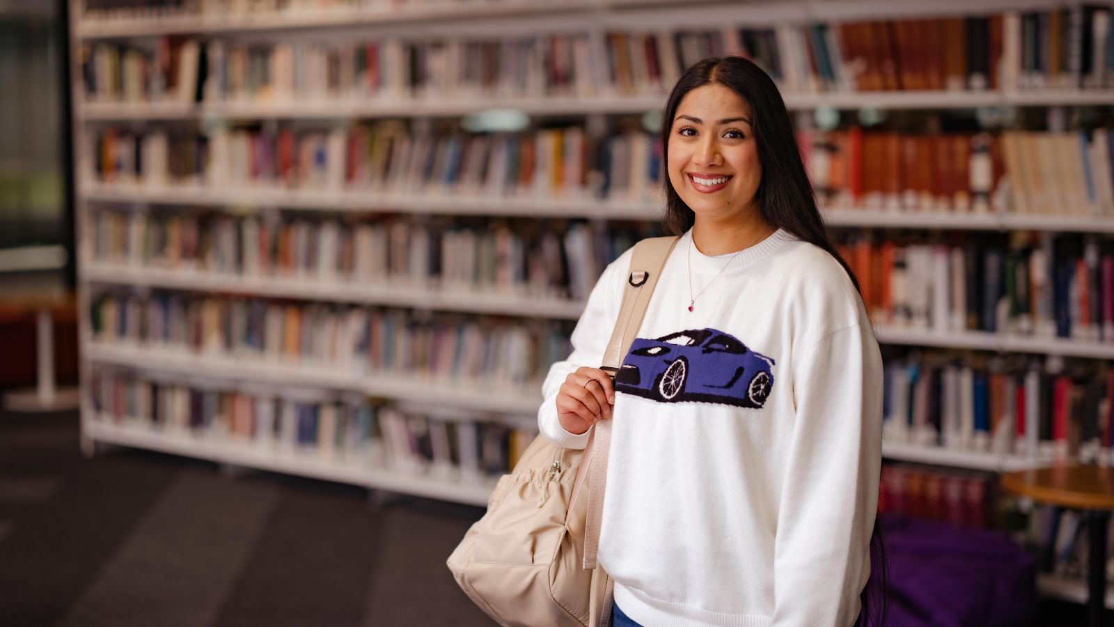 Alumni appeal scholarship recipient Bhavika stands in front of book shelves in the university library