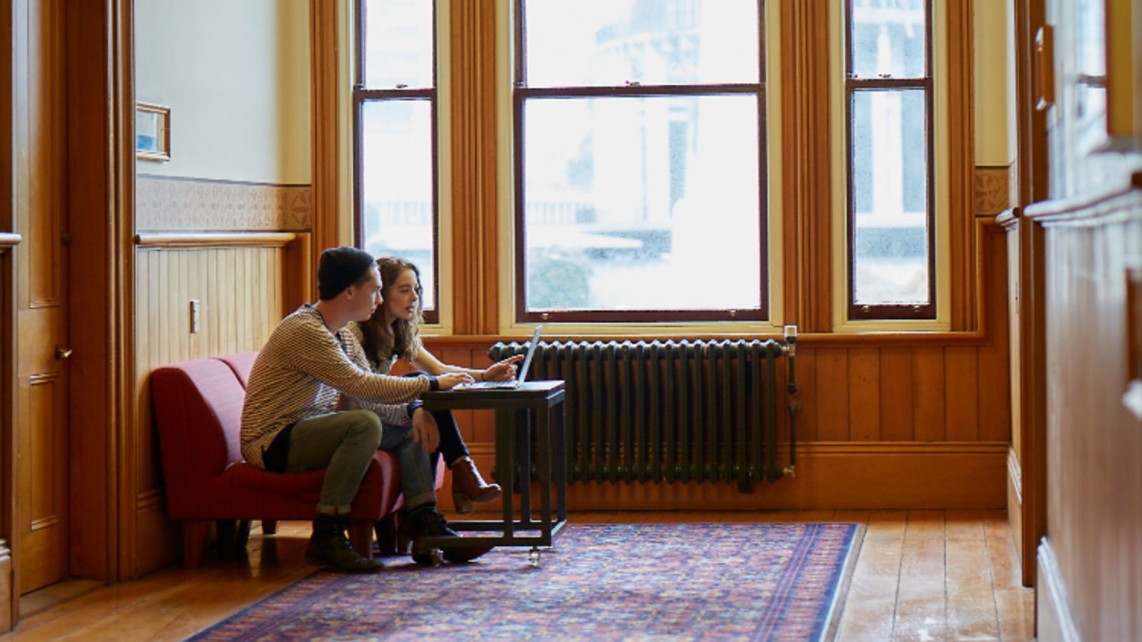 A male and a female Law student sit by the window of the Old Government Building with a laptop