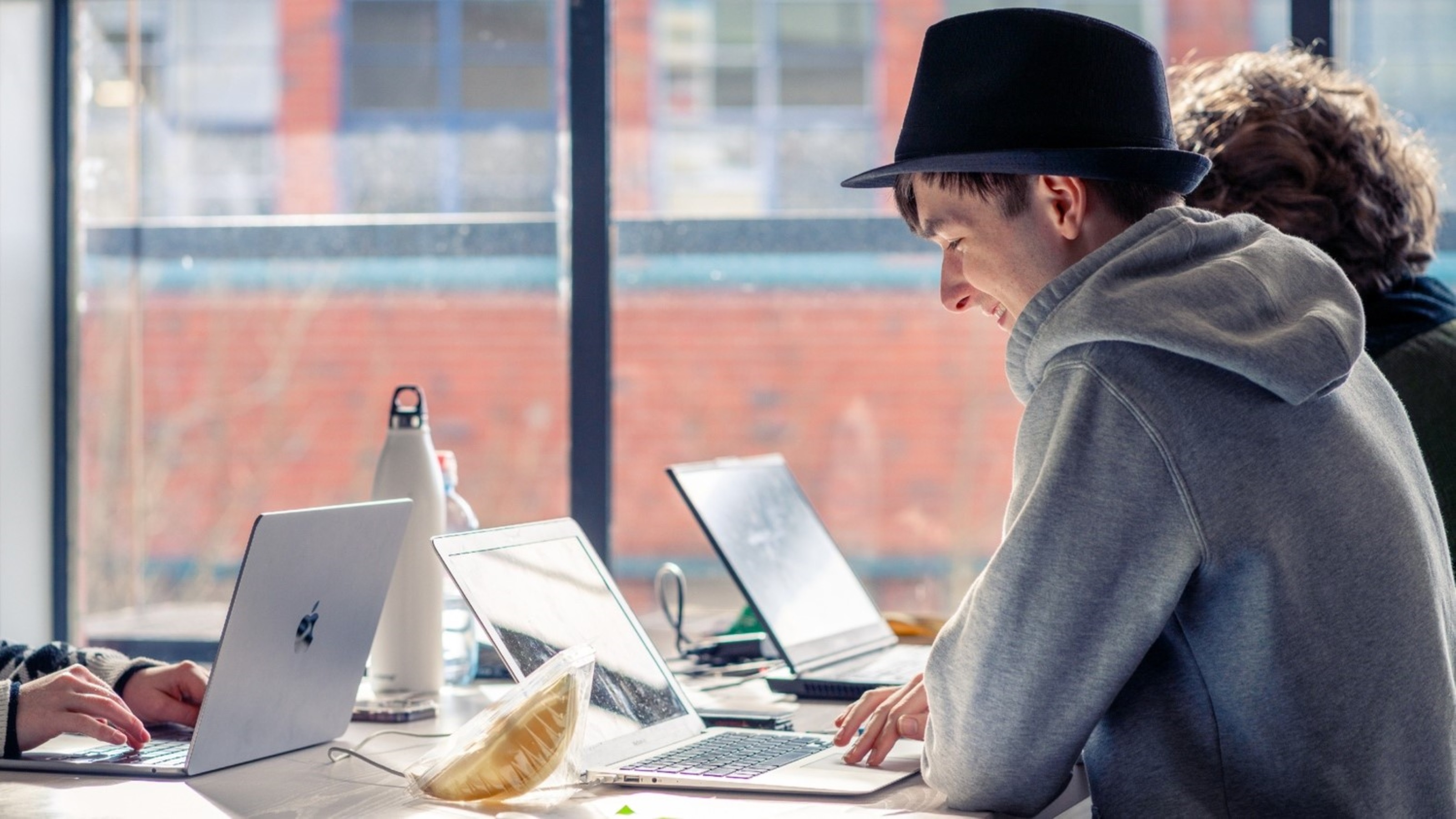 Several students using laptops at a shared study table beside large windows in the Kelburn Library at Te Herenga Waka—Victoria University of Wellington.