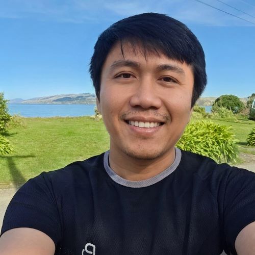 A person in a black t-shirt smiling, standing in front of a landscape view. 