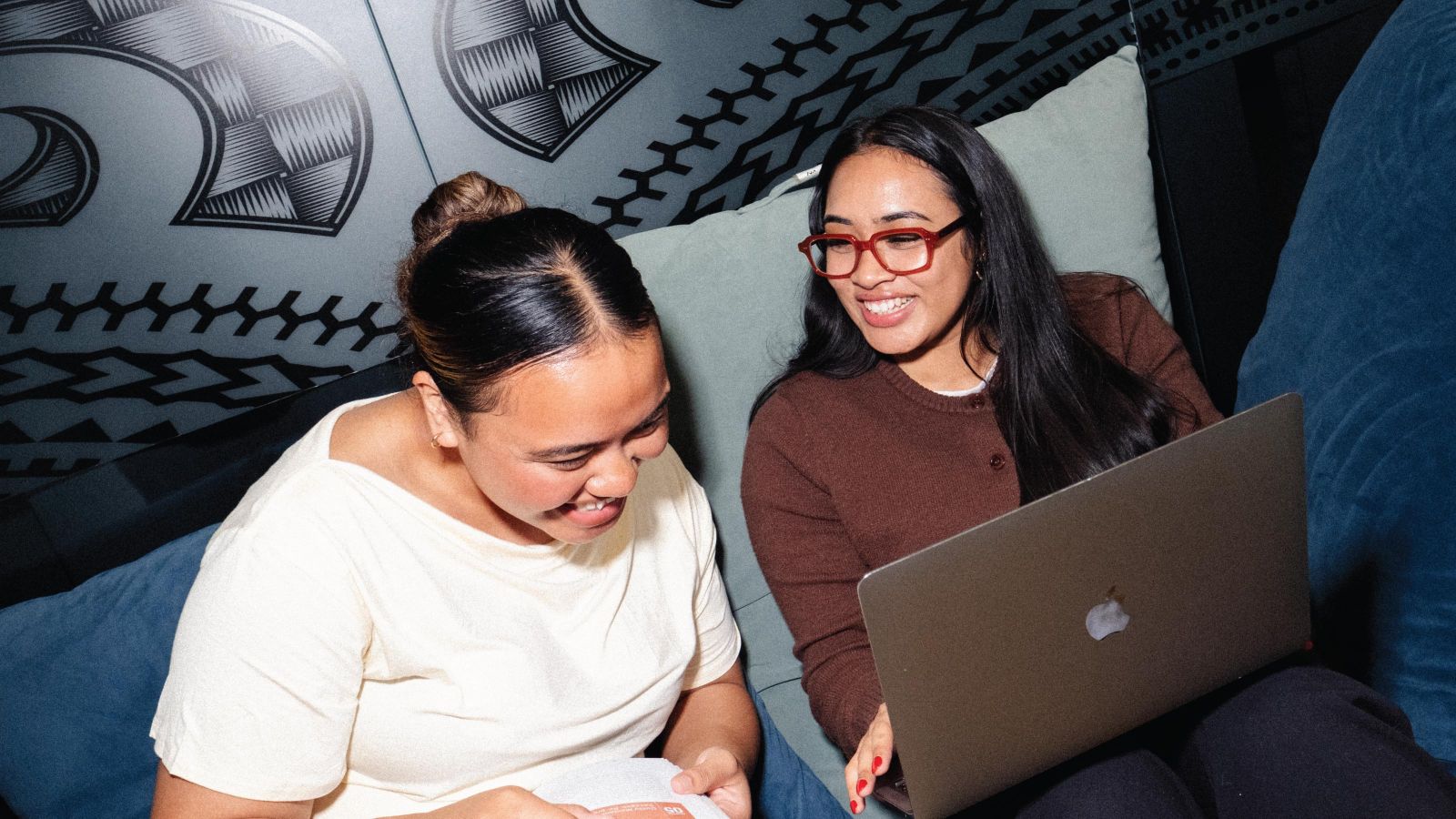 Two female students sitting down and laughing with a laptop