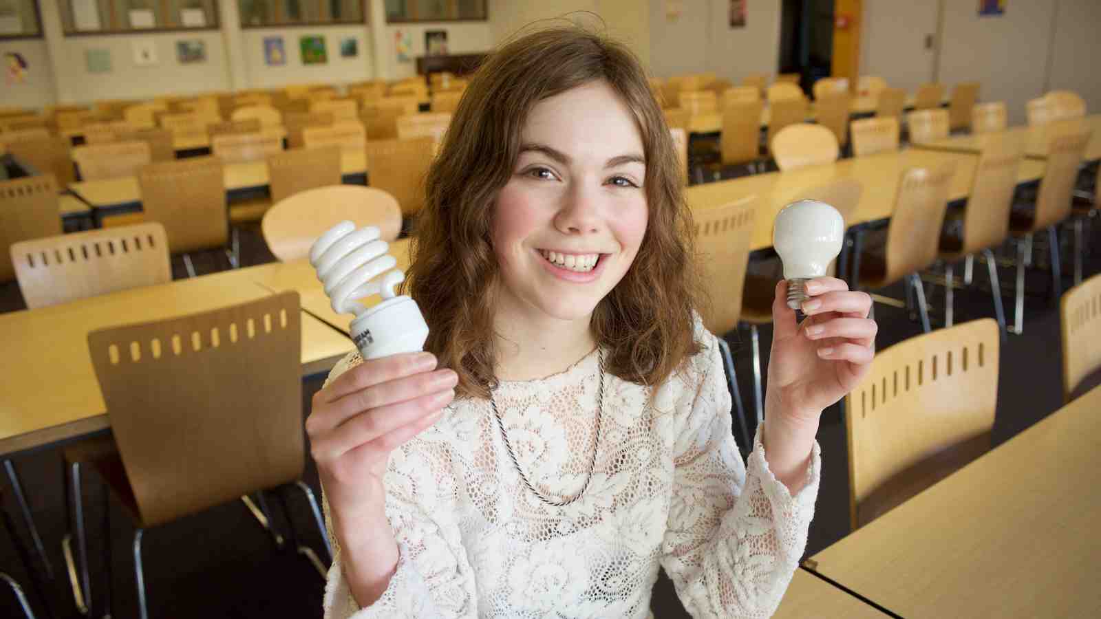 Bethany Paterson sits at a desk holding two lightbulbs