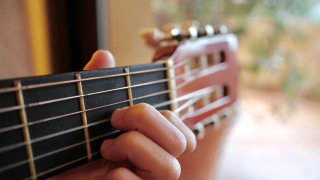 A hand playing chords on the neck of a guitar.