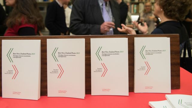 A view of four books with people talking in the background.