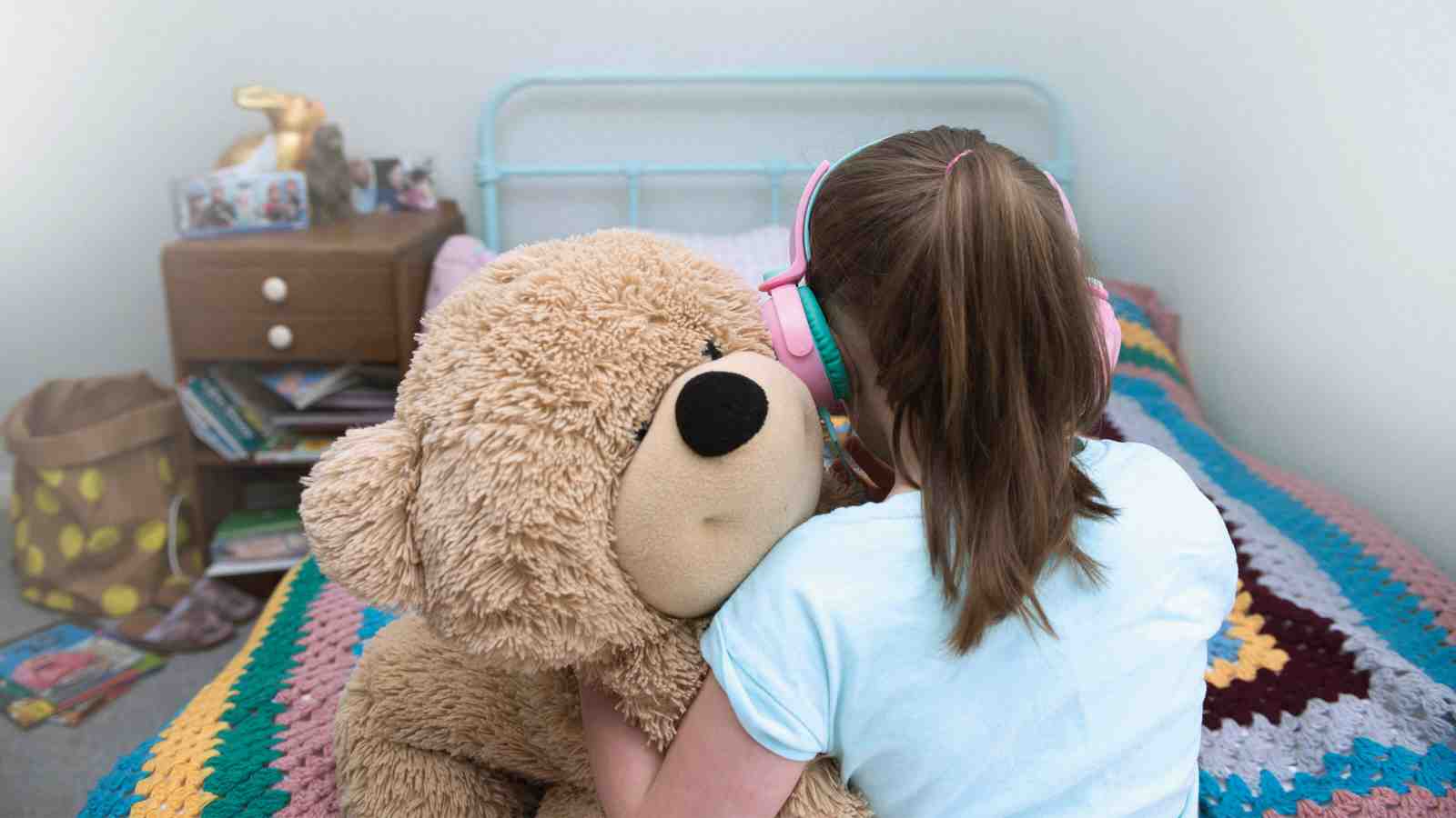 Girl holding her stuffed teddy bear toy while sitting on her bed