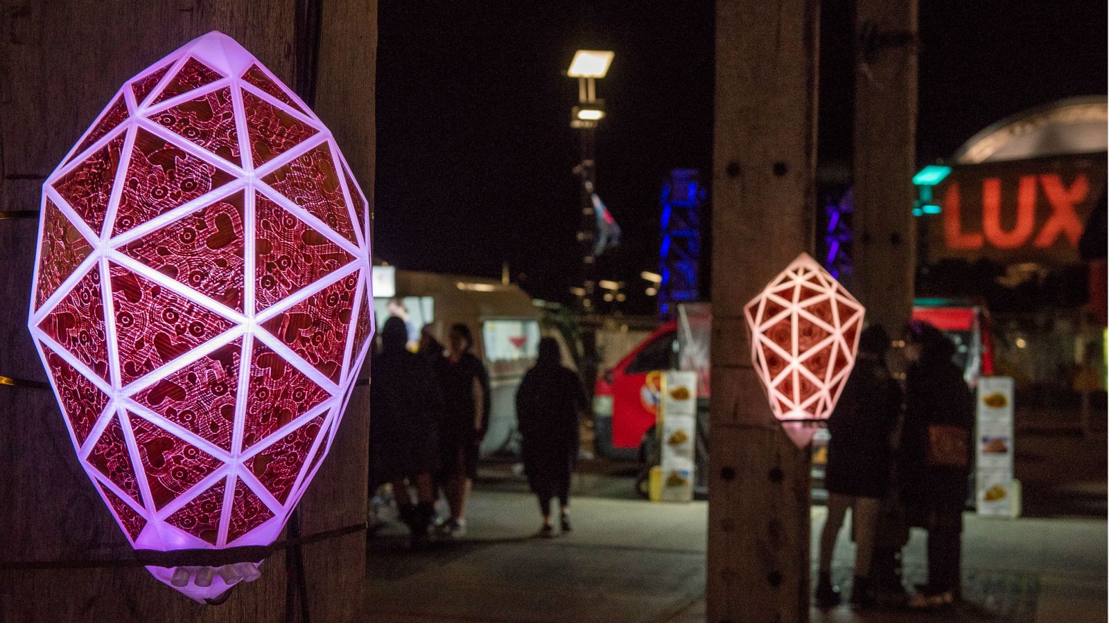 nga-tautiaki-lux.jpg Geometric lights glow at night on wooden poles in the city.