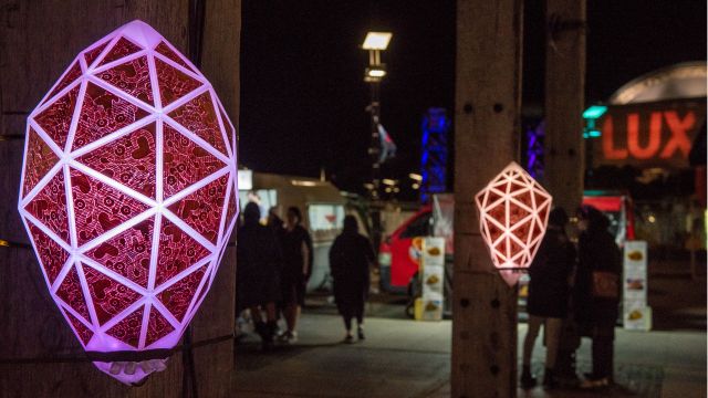 Geometric lights glow at night on wooden poles in the city.