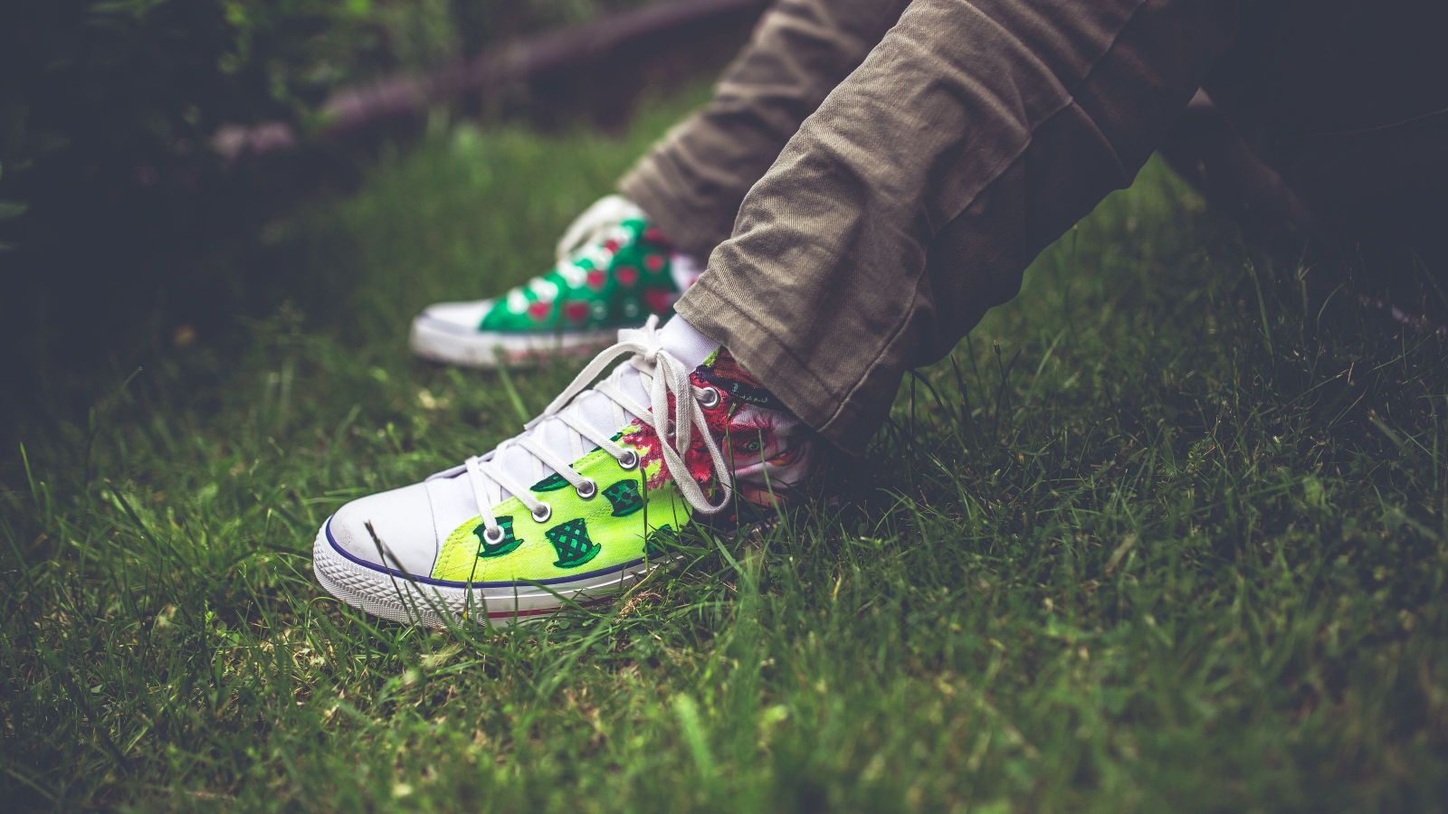 white and green sneakers worn by someone sitting with their feet on the lawn, close up of the feet