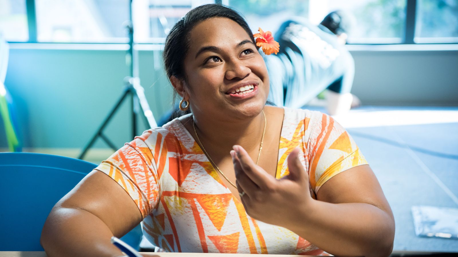 Scholarship – a pasifika woman smiles wearing an orange dress and an organge flower in her hair.