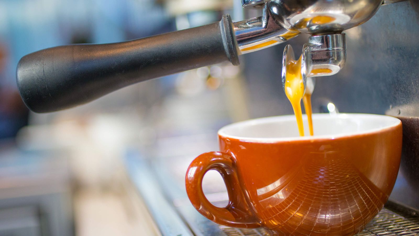 Espresso beginning to stream from a portafilter’s snout into a red ceramic mug.