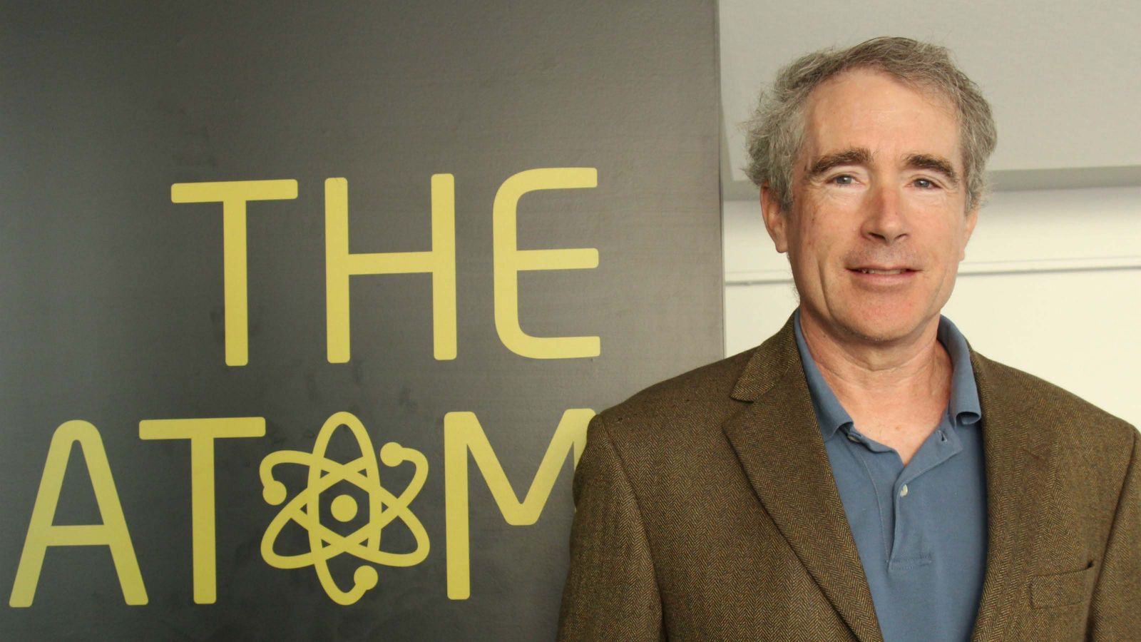 A profile shot of Michael Keefe, standing by a banner that reads, The Atom.