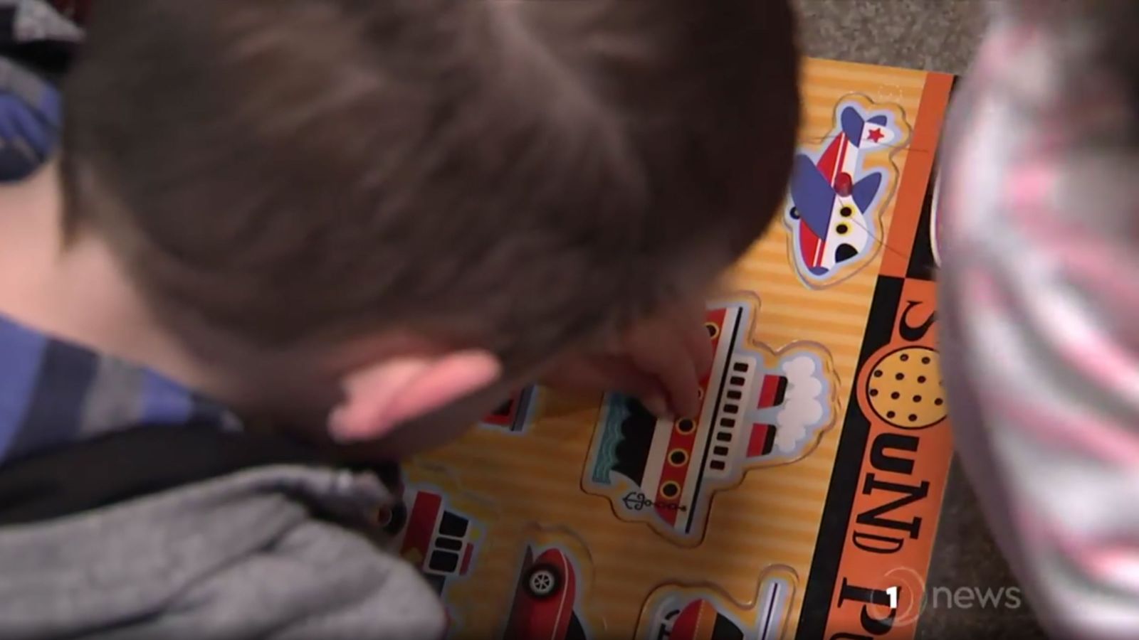 A child places a wooden ship puzzle piece into a puzzle.