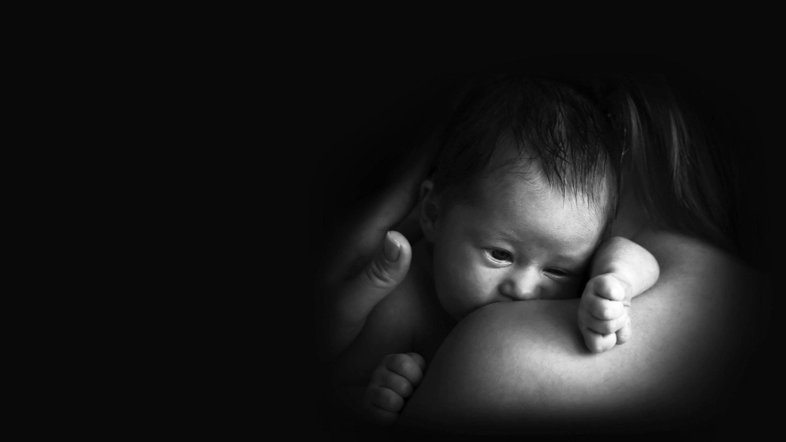 A newborn baby is being held by his mother and snuggling into her shoulder.