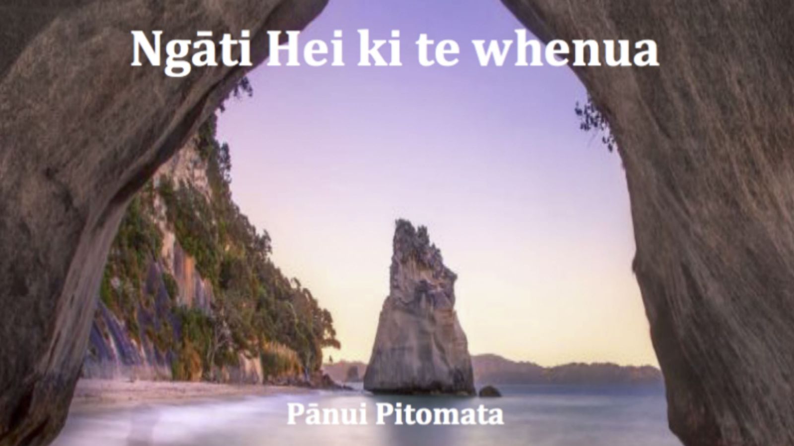 An image taken through a rocky arch on the shoreline of the ocean, looking out at a tall rock beside a sttep hill, under a purple sky, with text that reads, Ngāti Hei ki te whenua, Pānui Pitomata.