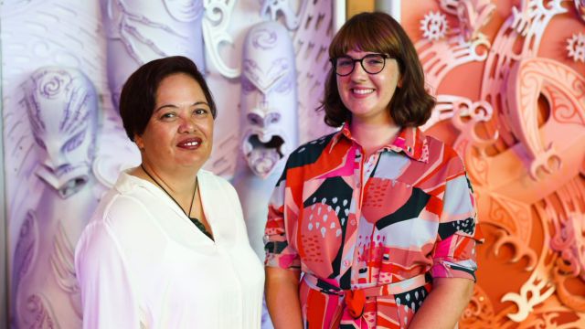 Museum and Heritage Studies Masters students and 2019 Te Papa Memorial Scholarships recipients Laureen Sadlier and Jessie Bray Sharpin, stand together in front of creative art.