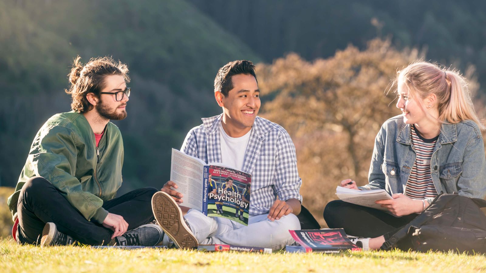 Three students sitting on a lawn and studying together on a sunny day.
