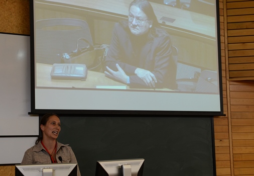 A professional woman stands at the front of a lecture hall and gives a presentation.