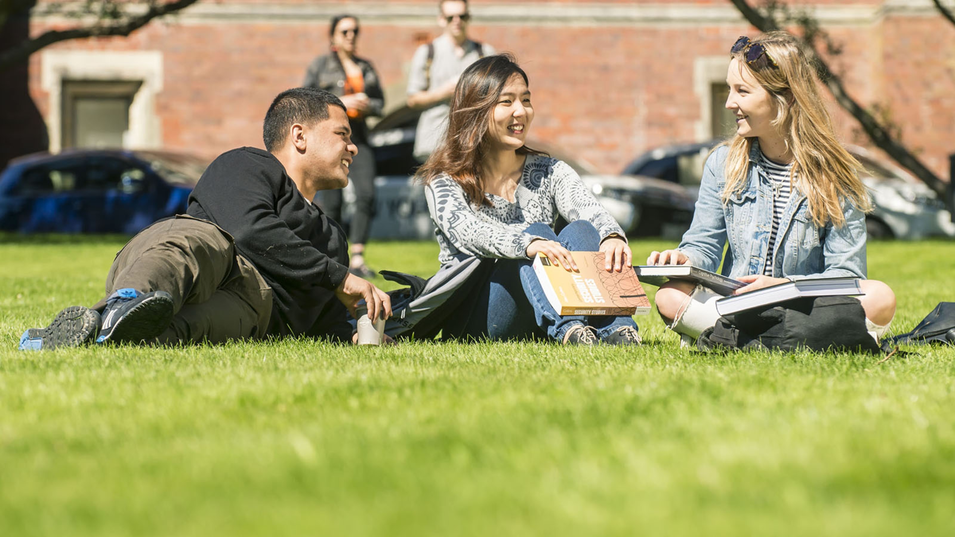 Three students are smiling and chatting on a lawn in Wellington.