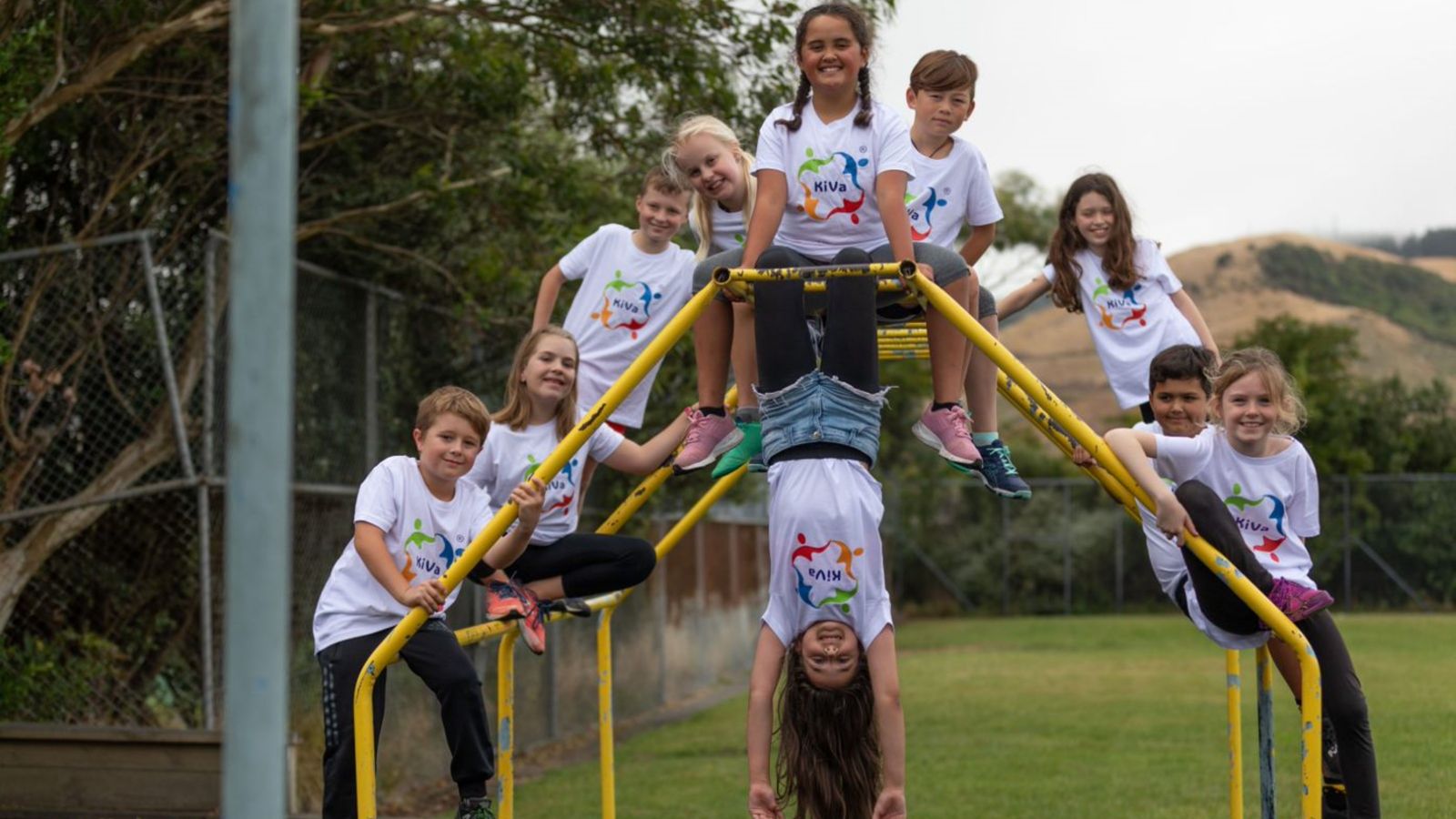 10 children posing on a yellow climbing frame, wearing white KiVa logo printed Tshirts